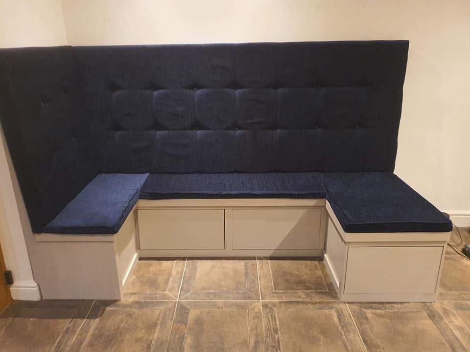 Built-in banquette seat with tall buttoned navy upholstered back and painted base with storage