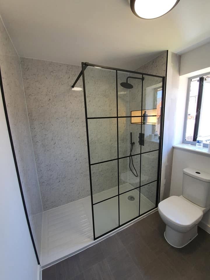 Walk-in shower with black grid-framed glass screen, marble-effect wall panels and matt black rain shower