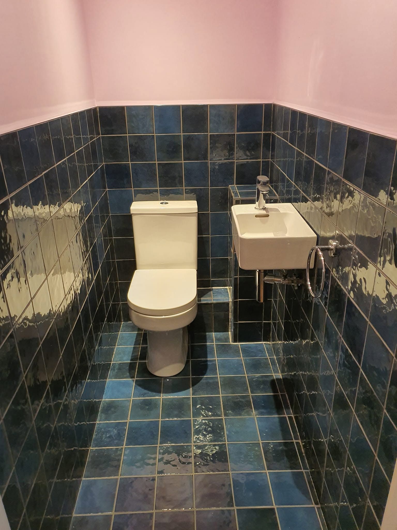 Cloakroom with glossy blue tiles on floor and lower walls, white toilet, small basin and pink upper walls