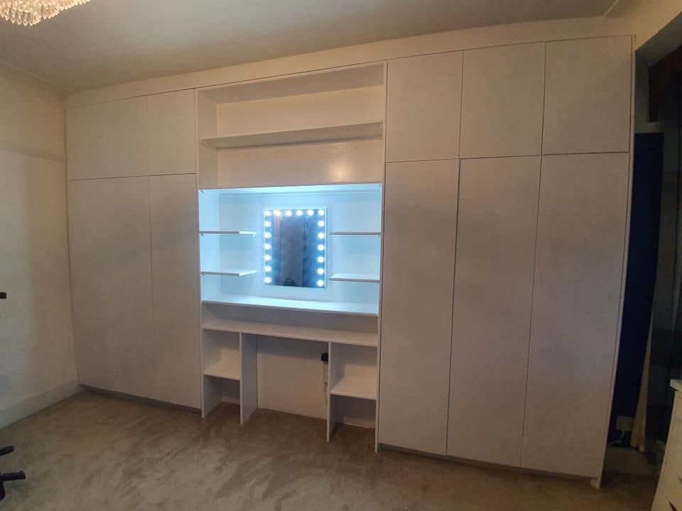 White floor-to-ceiling fitted wardrobes with built-in lit dressing table and Hollywood mirror
