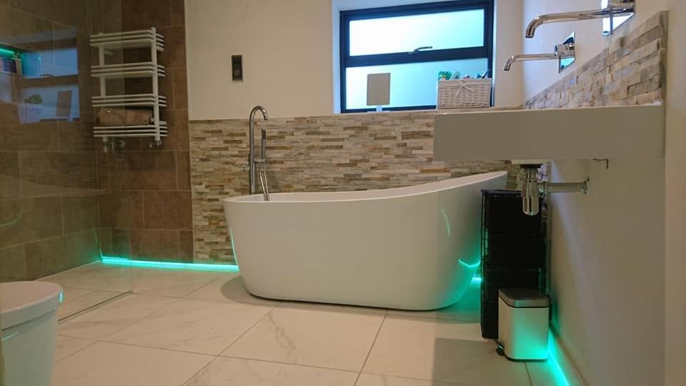 Freestanding white bath with floor-standing tap, split-face stone tiles and green LED floor-level lighting