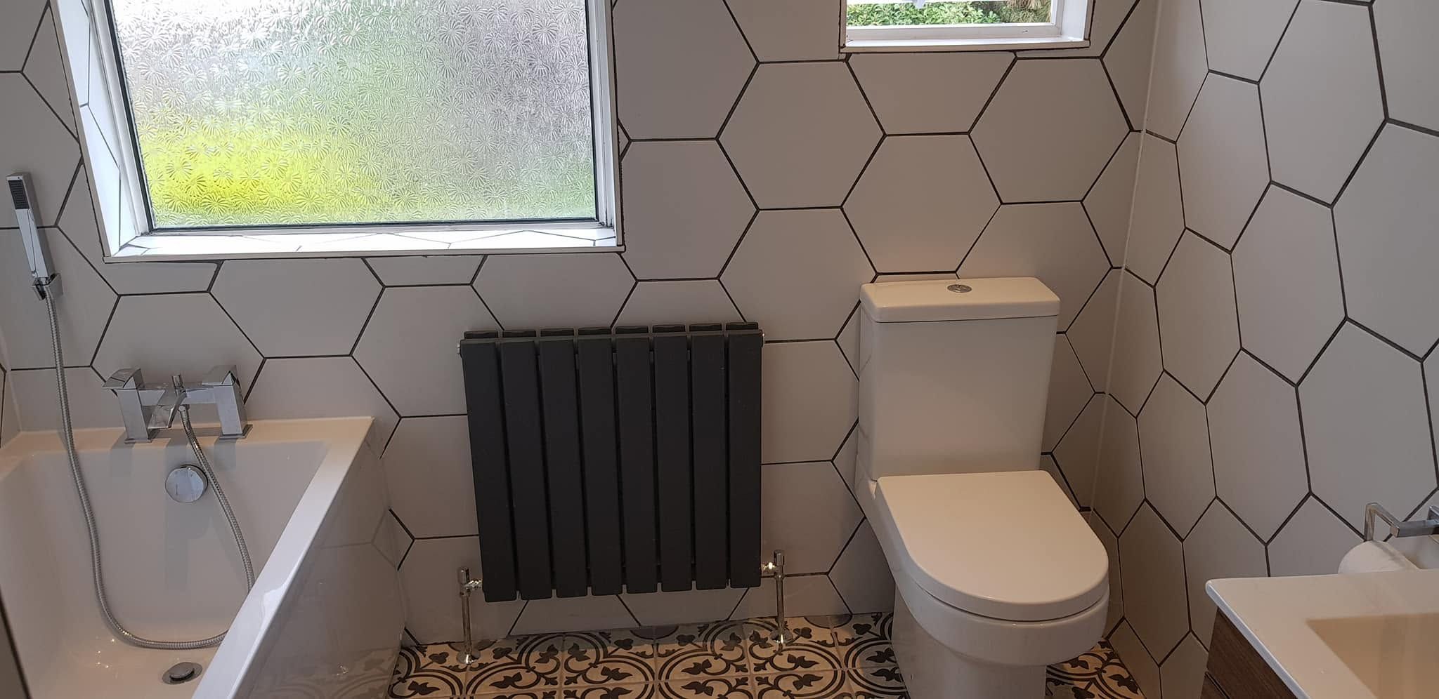 Bathroom with large white hexagon wall tiles, anthracite radiator, bath, toilet and black-and-white patterned floor tiles
