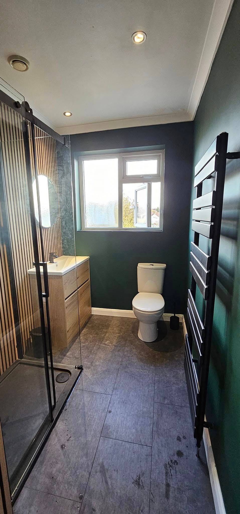 Shower room with dark green walls, oak slat feature wall, black shower enclosure and towel radiator
