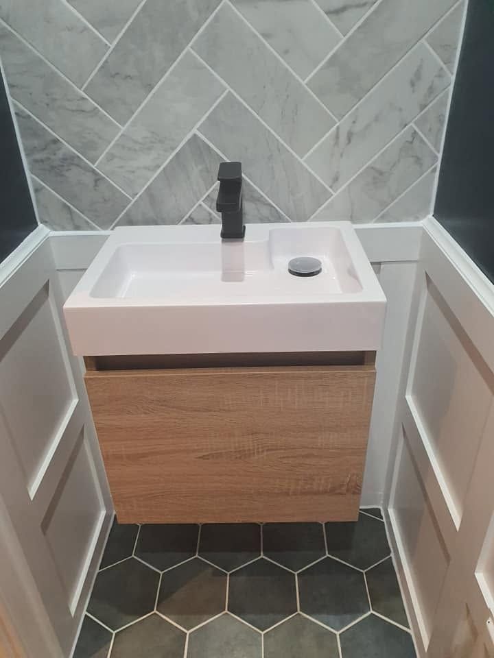 Compact oak-effect vanity with black tap between white panelled walls, herringbone tiles and dark hexagon floor