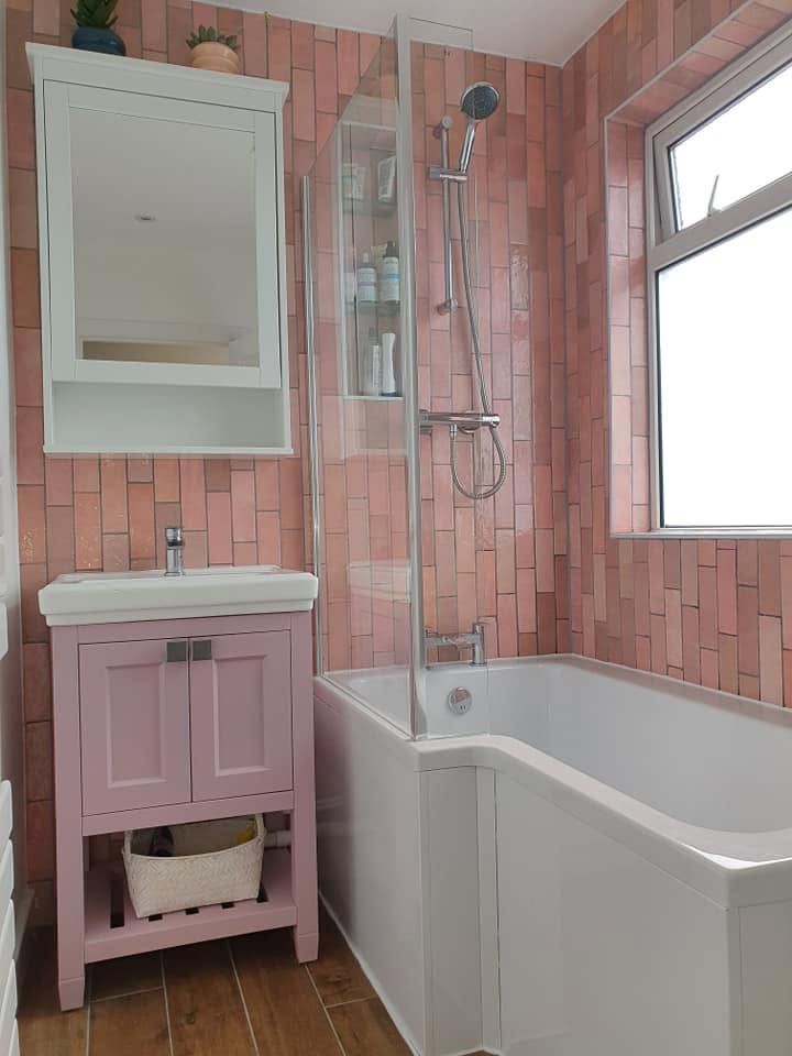 Bathroom with pink brick-effect wall tiles, P-shaped shower bath, pink vanity unit and white mirror cabinet