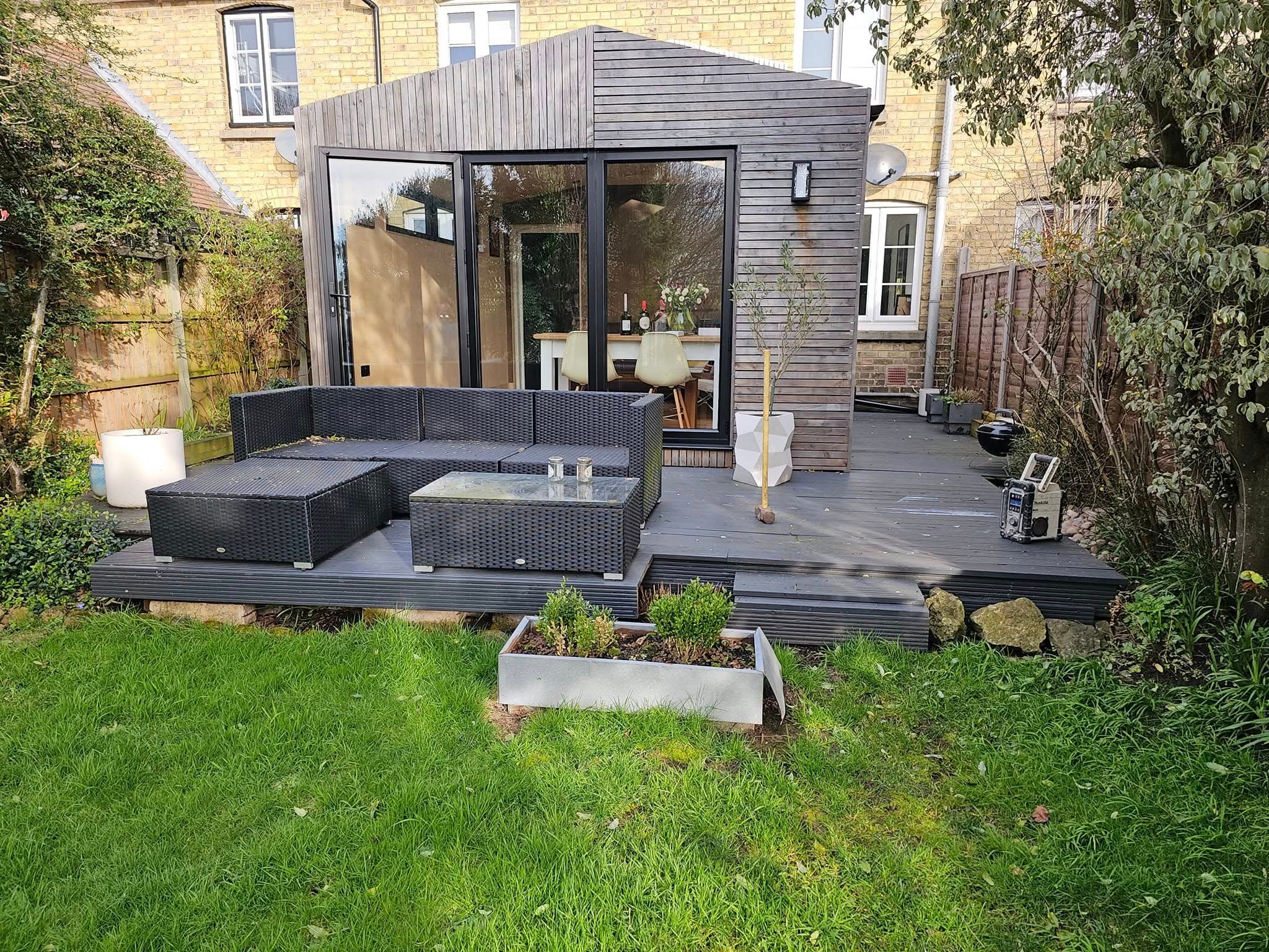 Grey composite decking with rattan sofa in front of a slatted timber garden room