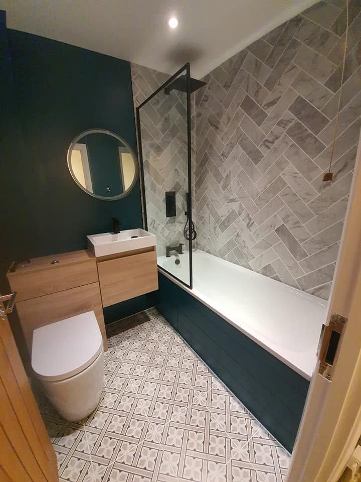 Bathroom with herringbone marble-effect tiles, teal panelled bath, black shower screen and patterned floor tiles