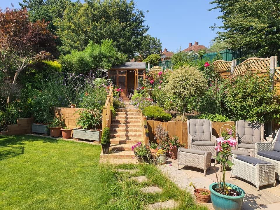 Terraced garden with brick and sleeper steps, sandstone patio, rattan chairs and lawn