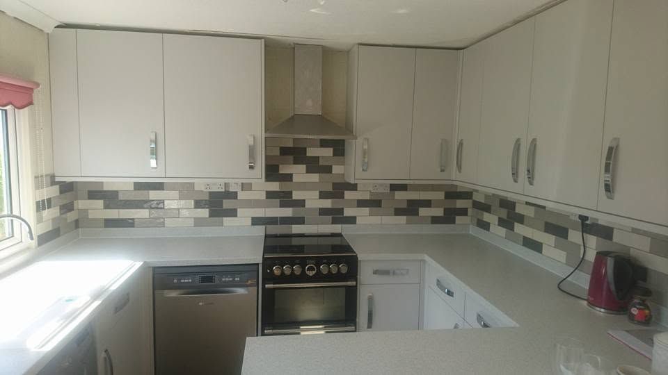 U-shaped kitchen with light grey gloss units, chimney extractor, range cooker and multi-tone tile splashback