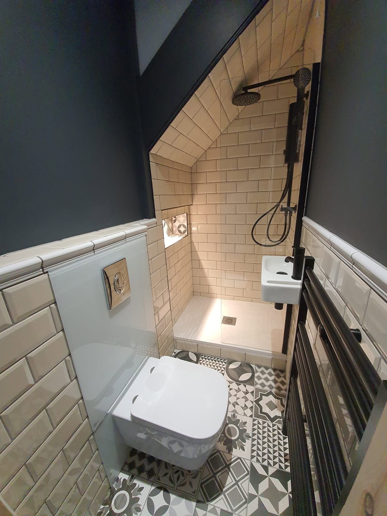 Shower room under the stairs with cream metro tiles, black rain shower, wall-hung toilet and patterned floor tiles