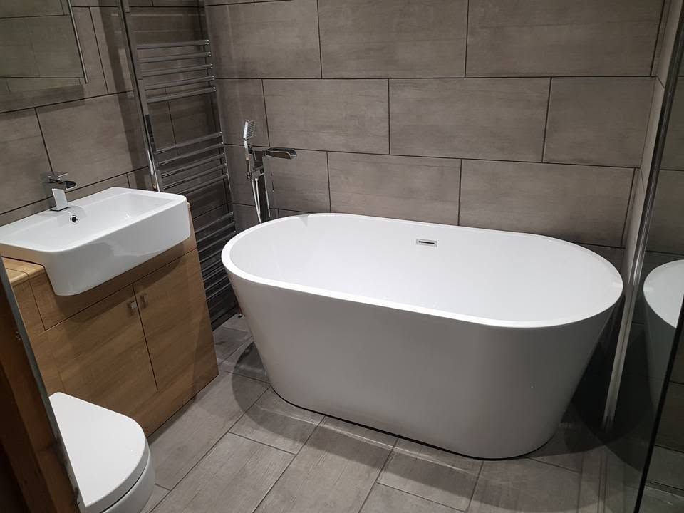 White freestanding bath with floor-standing chrome filler, oak-effect vanity unit and large grey wall and floor tiles